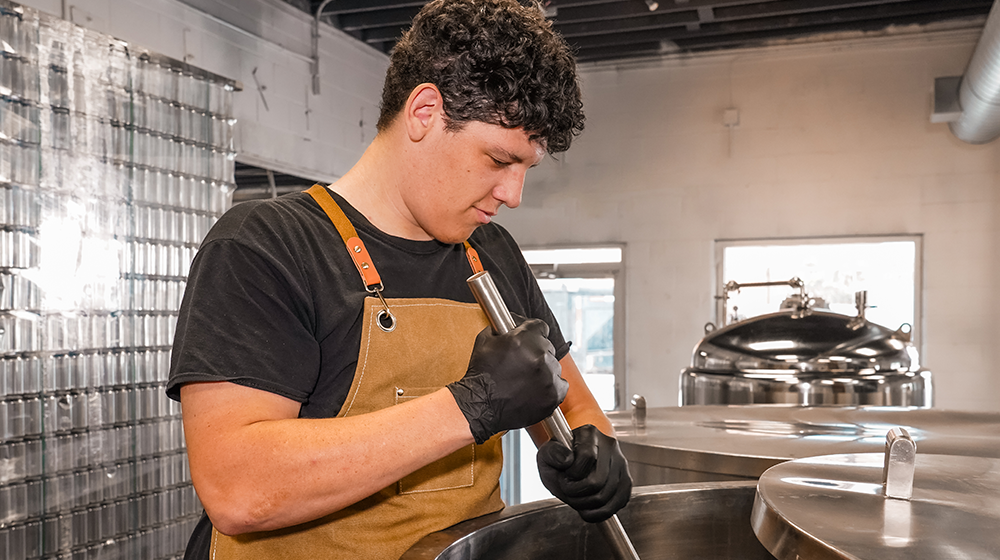 Brewery worker stirring stainless steel fermentation tank during kombucha brewing process at Firefly Brew.