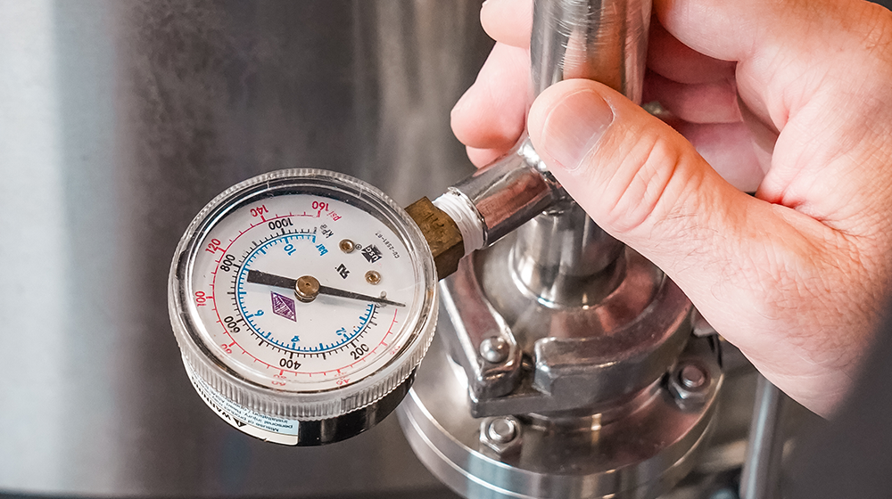 Pressure gauge and valve on stainless fermentation vessel being adjusted by a brewer.