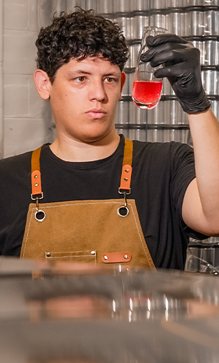 Person in apron analyzing kombucha in a glass